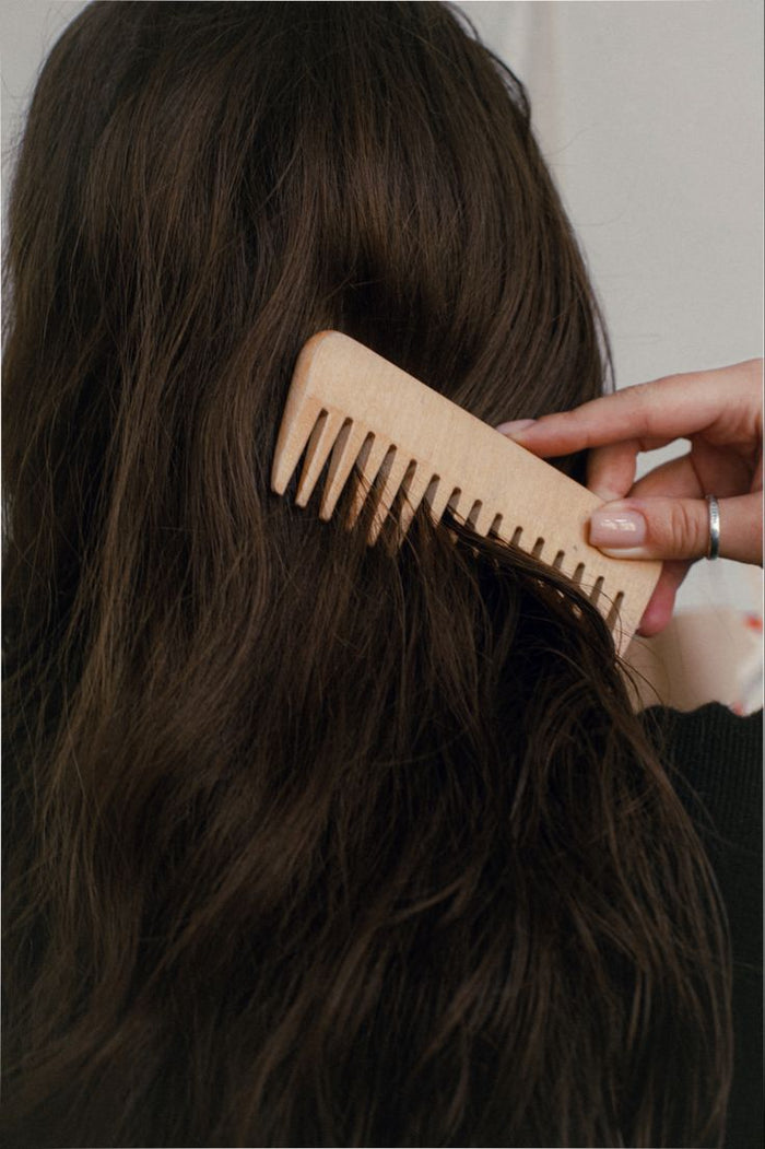 Femme se peignant les cheveux bruns avec un peigne en bois