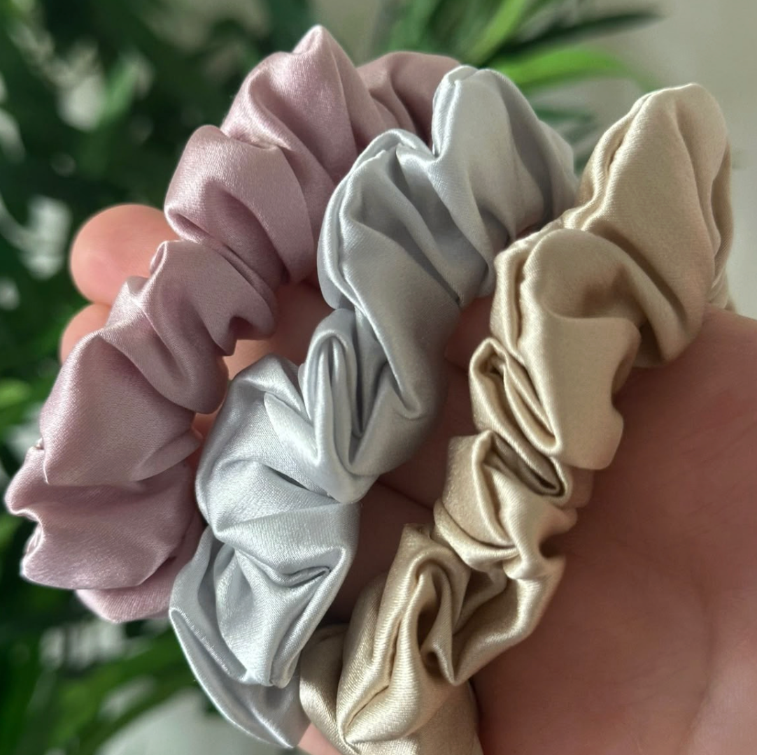 Trois chouchous en soie rose poudré, gris clair et beige tenus dans la main