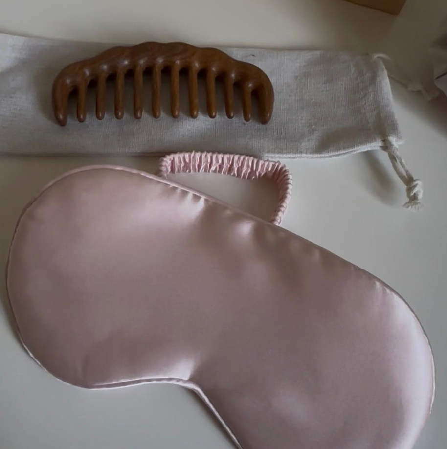 Masque de nuit en soie de mûrier rose poudré posé sur une pochette en lin avec un peigne en bois