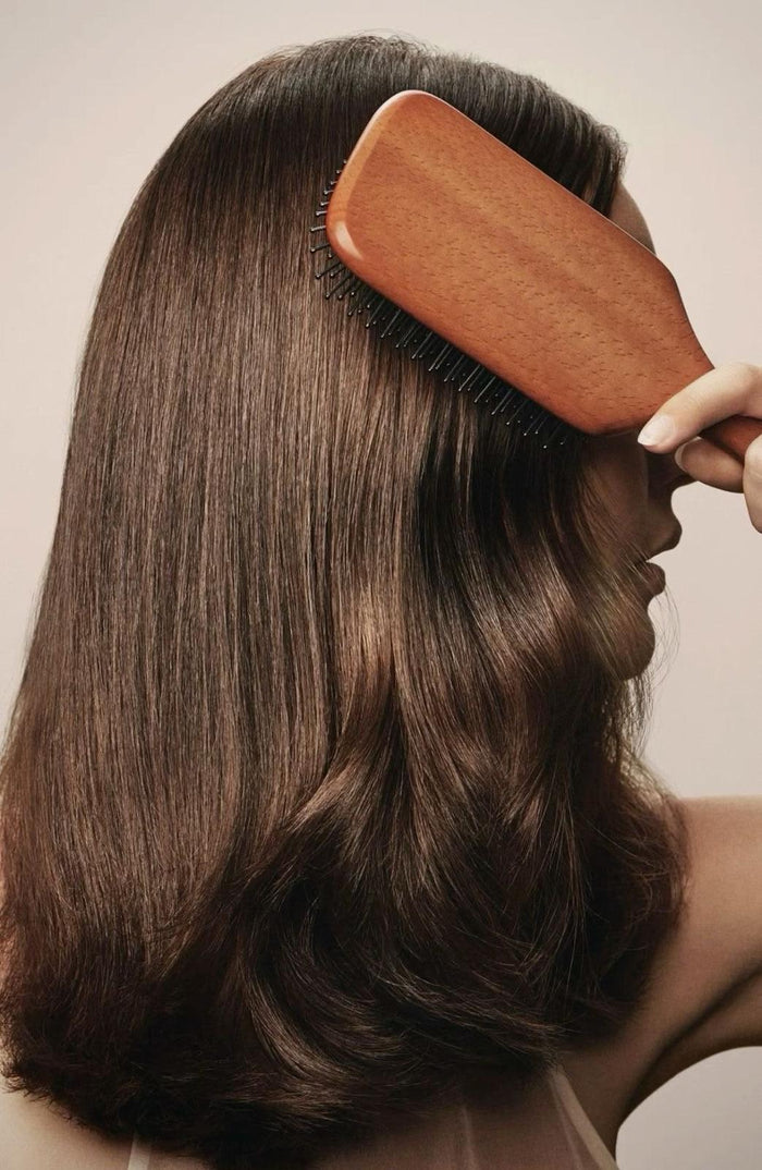 Femme se brossant des cheveux bruns lisses et brillants avec une brosse en bois