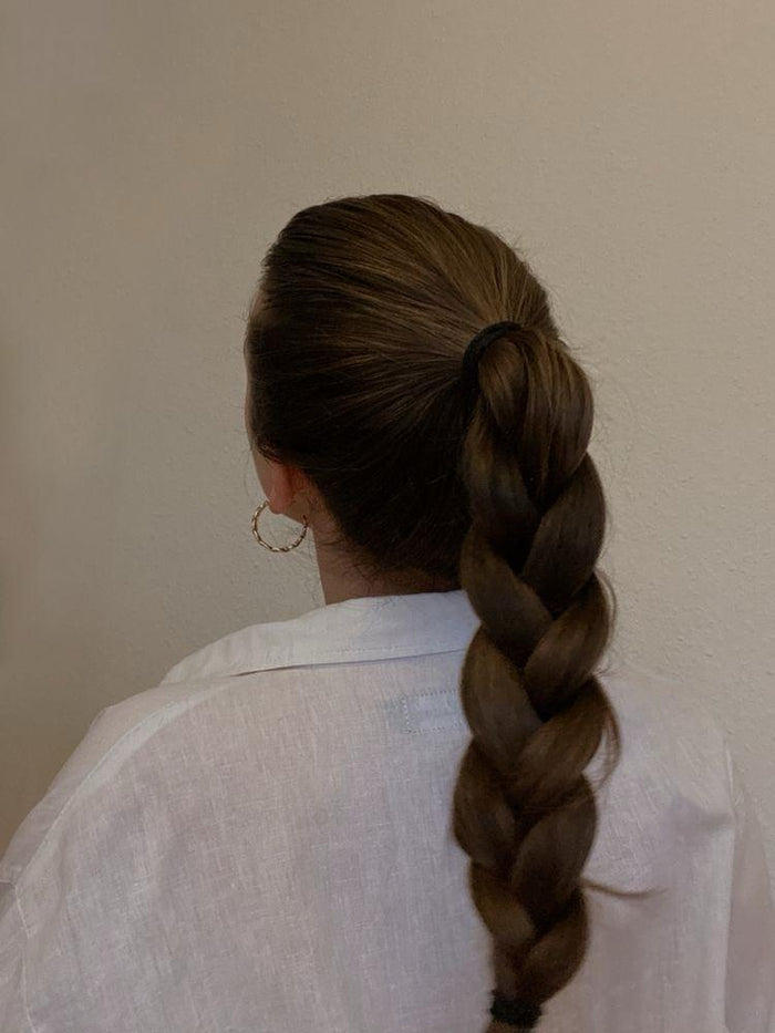 Femme de dos avec une longue tresse brune et une chemise blanche