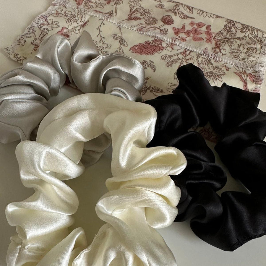 Trio de chouchous en soie gris perle, ivoire et noir posés sur un tissu fleuri