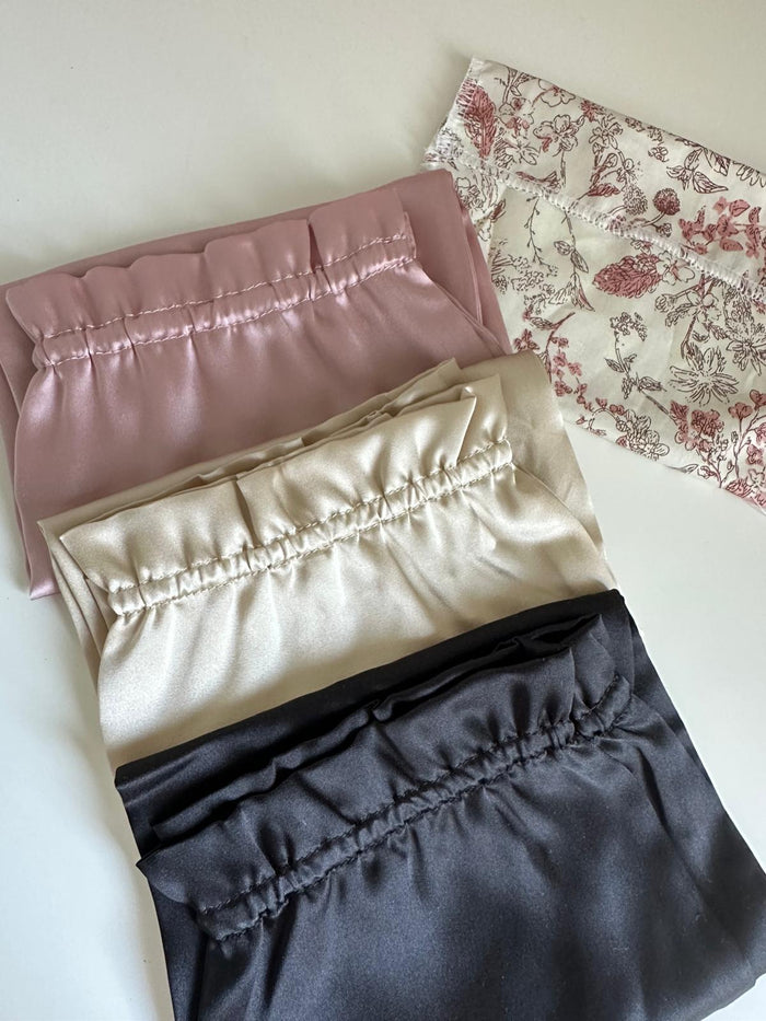 Trois bonnets de nuit en soie rose poudré, champagne et noir à plat près d'une pochette fleurie